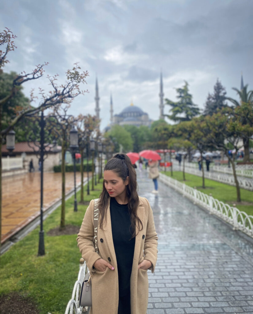 3 Days in Istanbul, Turkey Jet Lag Jelly creator wearing a camel coat on a rainy day in Sultanahmet Square with the Blue Mosque background