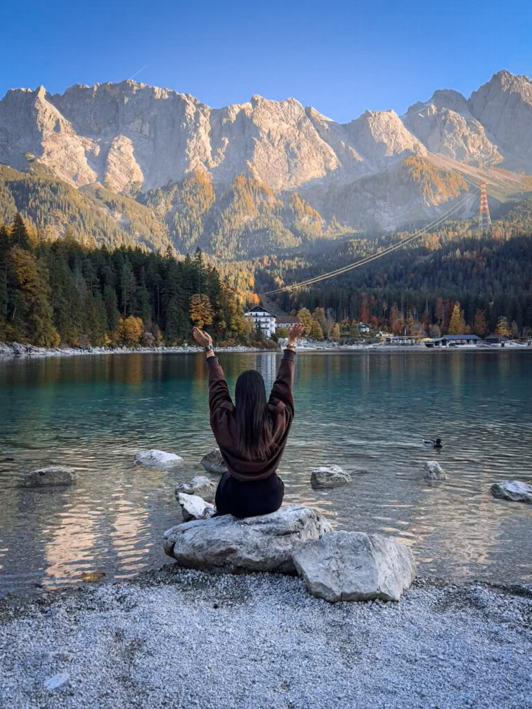 3 Days in Bavaria, Germany Sitting on rocks with arms raised looking across Lake Eibsee toward the Zugspitze mountains