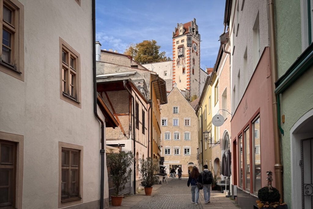 3 Days in Bavaria, Germany Hohes Schloss castle tower peeking above a colorful cobblestone street in Füssen Germany