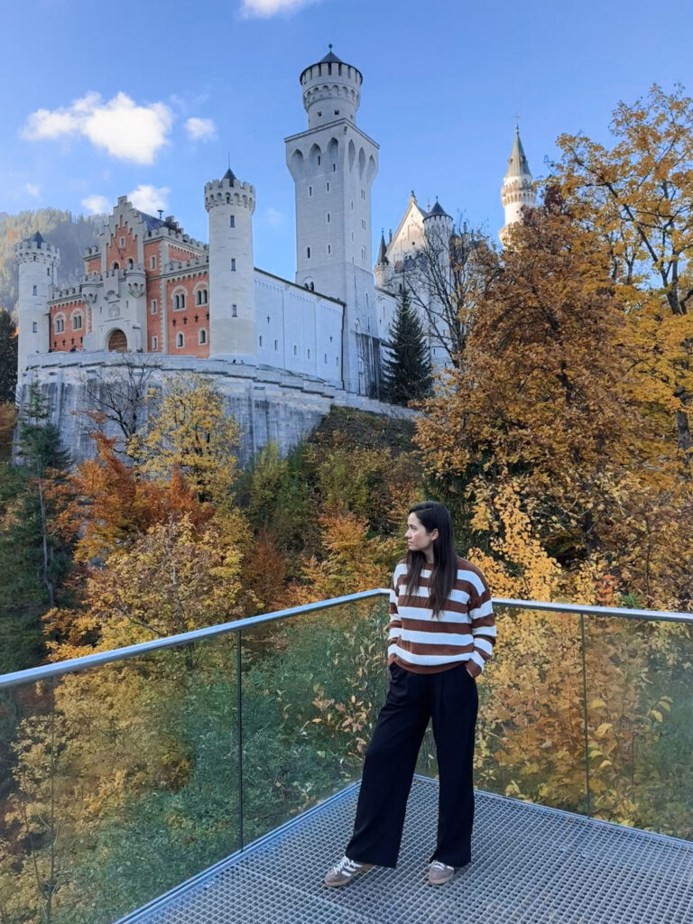 3 Days in Bavaria, Germany Traveler standing on a viewing platform looking up at Neuschwanstein Castle in autumn