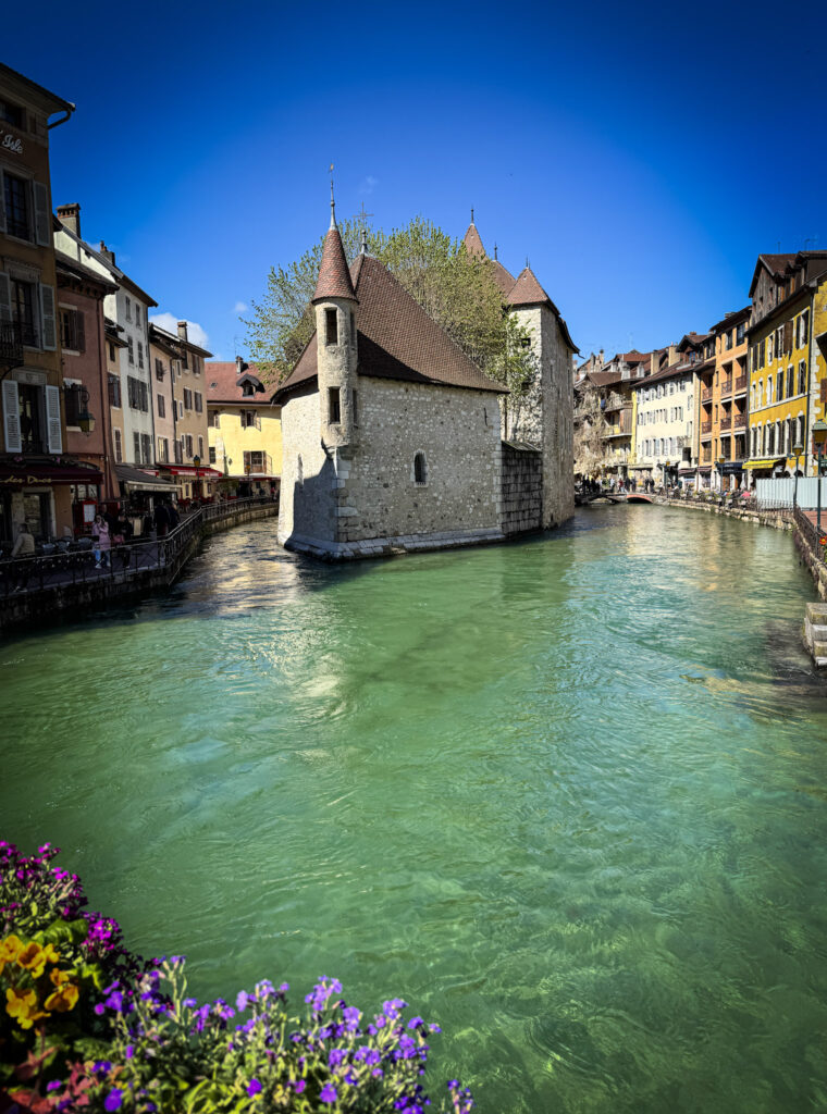 Top 10 Places in Southeastern France The historic stone Palais de l'Isle castle sitting in the center of the green Thiou River canal, surrounded by colorful old town buildings under a clear blue sky in Annecy, France
