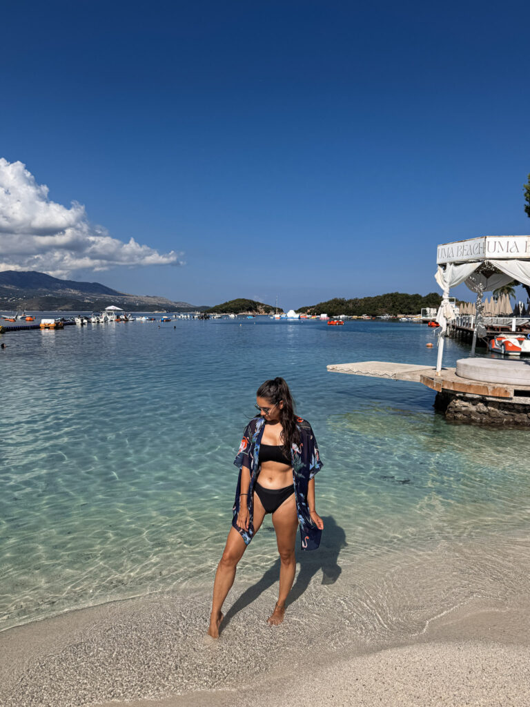Top 10 Beaches in Ksamil, Albania Blog author standing on the sandy shoreline of Bora Bora Beach over a crystal-clear turquoise bay in Ksamil, Albania.