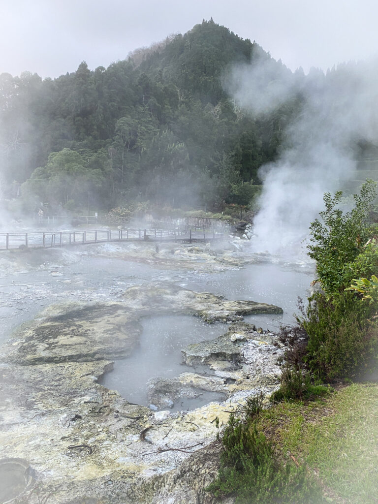 Top Things to Do in São Miguel, Azores Thick white steam rising from bubbling geothermal mud pools and hot springs at Caldeiras das Furnas, surrounded by a wooden boardwalk and lush green hills in São Miguel, Azores.