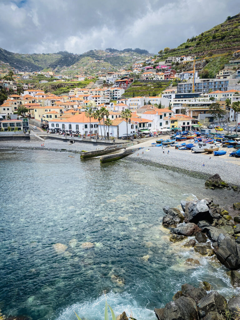 Madeira Travel Guide High-angle view of the clear turquoise bay and pebble beach of Câmara de Lobos fishing village in Madeira, dotted with colorful boats.
