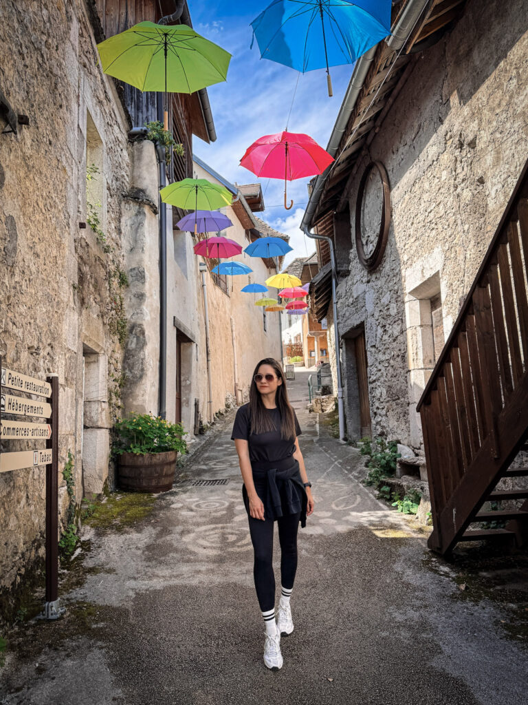 Top 10 Places in Southeastern France Traveler posing on a historic village street under the floating umbrella art installation in Chanaz, France