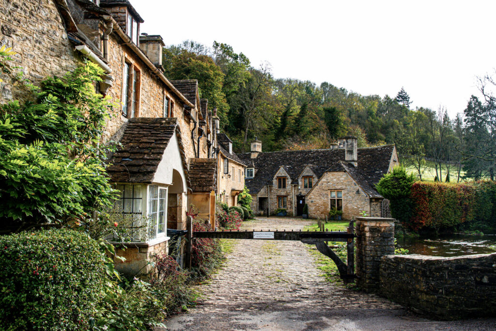 Top 5 Villages in the Cotswolds Historic limestone weavers' cottages and a gated cobblestone path next to the river in the village of Castle Combe.