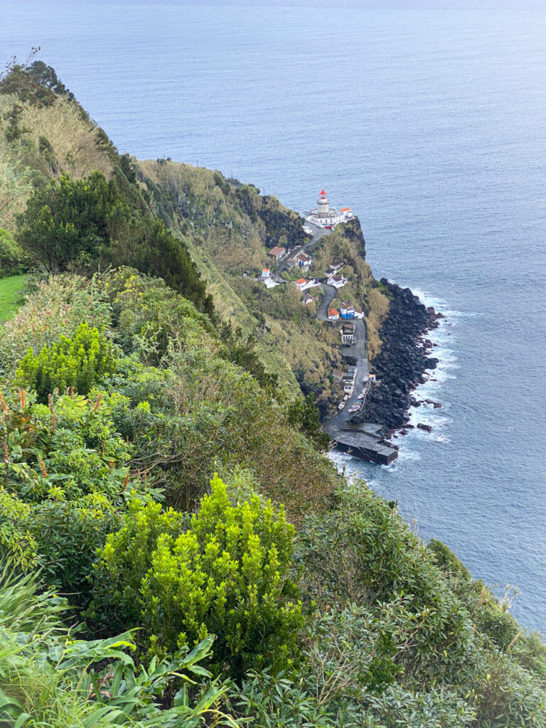 Top Things to Do in São Miguel, Azores A scenic coastal lighthouse clinging to a lush green mountain cliff next to the blue sea in the Azores.