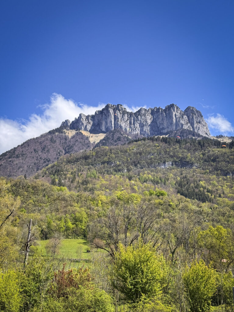 Top 10 Places in Southeastern France The jagged, rocky limestone peaks of the Dents de Lanfon mountain rise above a lush green forested hillside under a clear blue sky near Lake Annecy, France