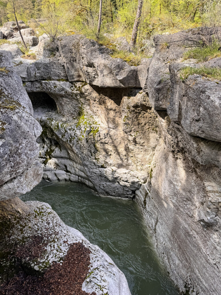 Top 10 Places in Southeastern France A rushing river cuts through a narrow, deep gorge with massive gray limestone rock formations and natural stone arches carved by water erosion at Gorges du Fier near Annecy, France