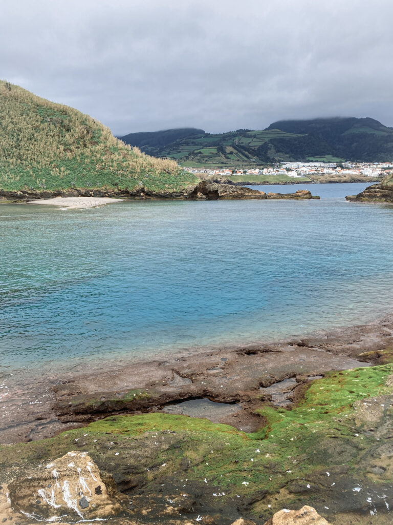 Top Things to Do in São Miguel, Azores Clear turquoise waters inside the volcanic crater lagoon of Vila Franca Islet, looking across the sea toward the coastal town and green hills of São Miguel, Azores.