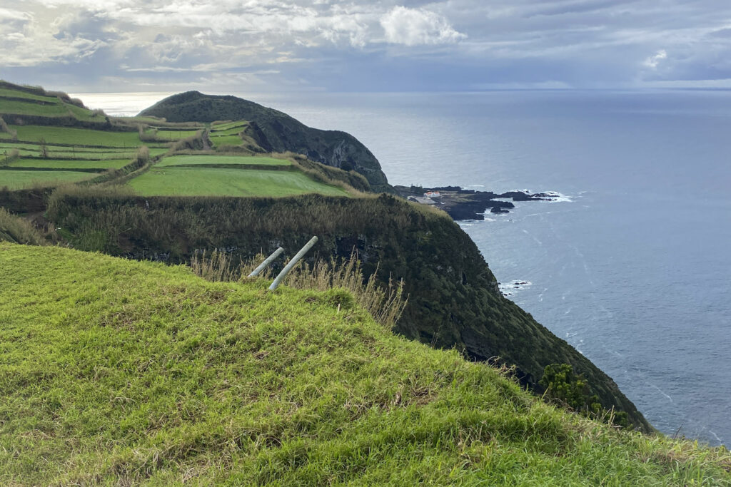 Top Things to Do in São Miguel, Azores Dramatic green sea cliffs and terraced farmland dropping into the Atlantic Ocean under a moody sky at Miradouro do Escalvado in São Miguel, Azores.