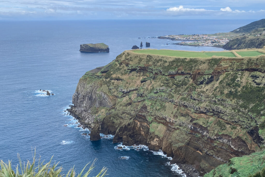 Top Things to Do in São Miguel, Azores Steep volcanic sea cliffs topped with green pastures overlooking the Atlantic Ocean and the distant sea stacks of Mosteiros in São Miguel, Azores.