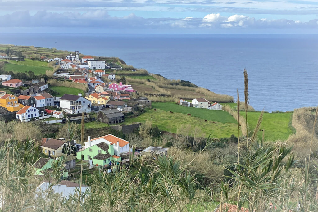 Top Things to Do in São Miguel, Azores High-angle view of colorful houses and green pastures cascading down sea cliffs in Ajuda da Bretanha, overlooking the Atlantic Ocean from Miradouro do Pico Vermelho, São Miguel, Azores.