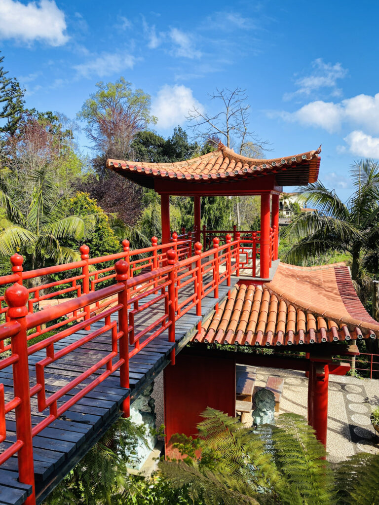 Madeira Travel Guide A bright red Asian-style pagoda and pedestrian bridge surrounded by lush green palm trees at Monte Palace Tropical Garden in Madeira.