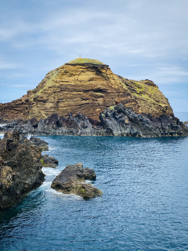 Madeira Travel Guide A massive volcanic rock islet rising from the blue ocean near the rocky coast of Seixal Beach, Madeira.