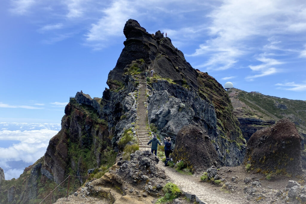 Madeira Travel Guide Hikers climbing a steep, narrow staircase built into a jagged volcanic ridge along the PR1 Vereda do Arieiro trail in Madeira.