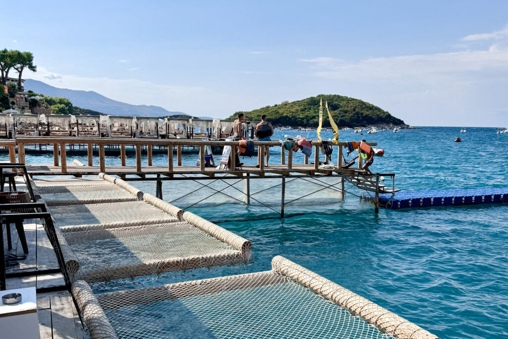 Top 10 Beaches in Ksamil, Albania Luxury overwater net hammocks built into a wooden deck overlooking the clear turquoise bay at Orange Beach Club in Ksamil, Albania.
