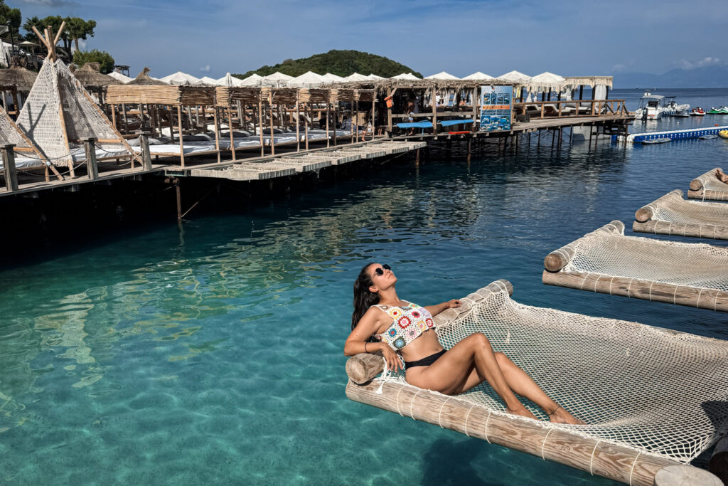 Top 10 Beaches in Ksamil, Albania Sunbathing on a luxury overwater net hammock over crystal-clear turquoise sea at Poda Beach Club in Ksamil, Albania.