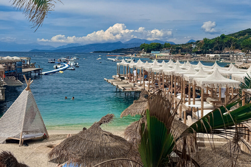 Top 10 Beaches in Ksamil, Albania Overwater wooden decks lined with white macrame sun cabanas and straw umbrellas at Poda Beach Club in Ksamil, Albania.