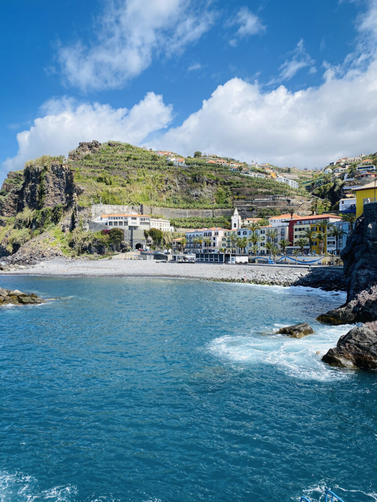 Madeira Travel Guide The colorful coastal village of Ponta do Sol in Madeira, nestled between a pebble beach and steep green cliffs under a blue sky