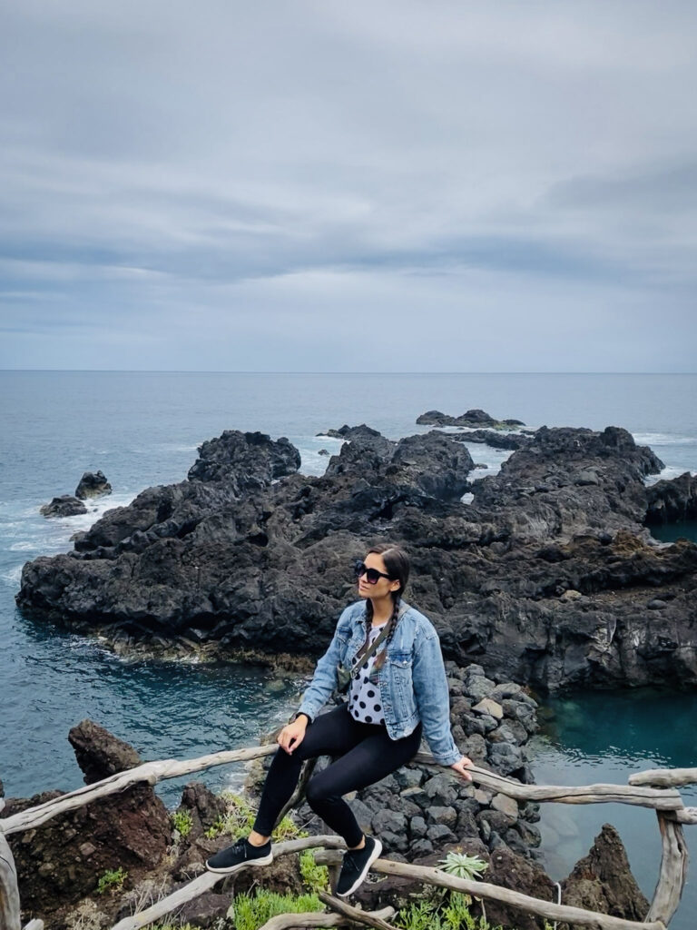 Madeira Travel Guide Traveler sitting at a scenic overlook of volcanic coastal rocks in Madeira.