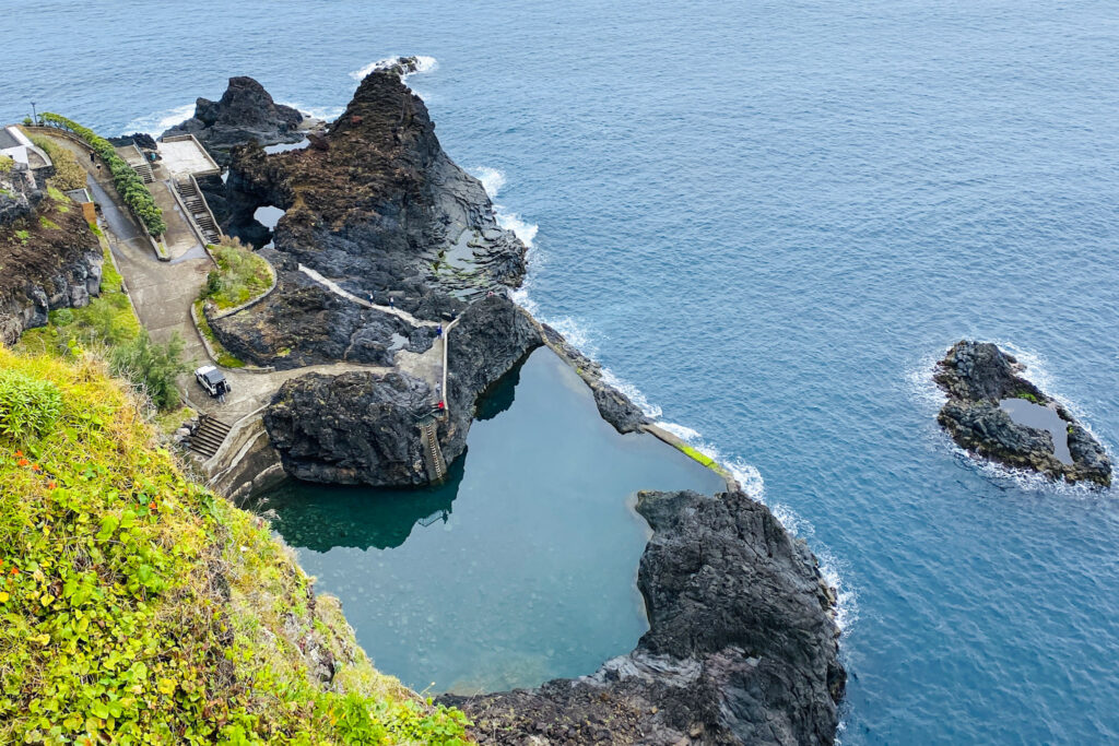 Madeira Travel Guide High-angle aerial view of a natural volcanic swimming pool nestled in the dark lava rock coastline of Seixal, Madeira.