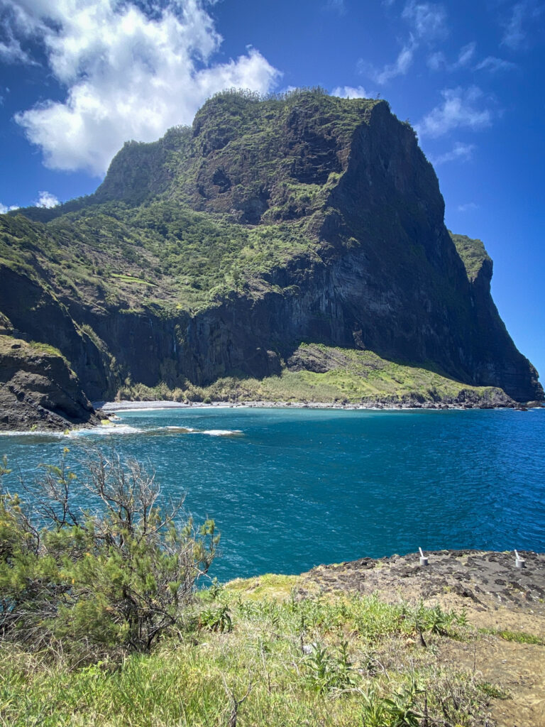 Madeira Travel Guide A close-up view of the massive Penha de Águia (Eagle Rock) mountain towering over a vibrant teal ocean bay in Porto da Cruz, Madeira.