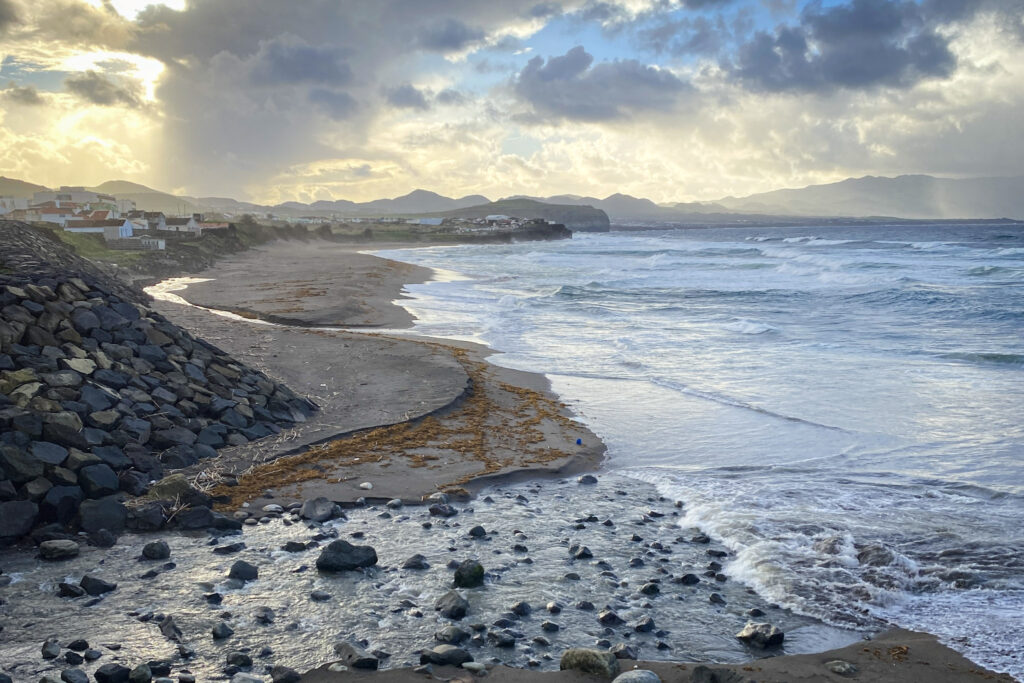Top Things to Do in São Miguel, Azores Dramatic sunset over the black sand beach and crashing waves of Praia do Monte Verde, with a rocky river mouth stream in the foreground in Ribeira Grande, São Miguel, Azores.