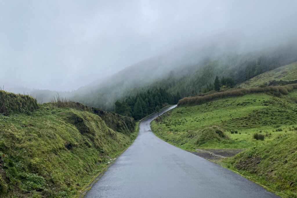 Top Things to Do in São Miguel, Azores Winding asphalt road cutting through lush green hills and misty, fog-covered mountains in São Miguel, Azores.