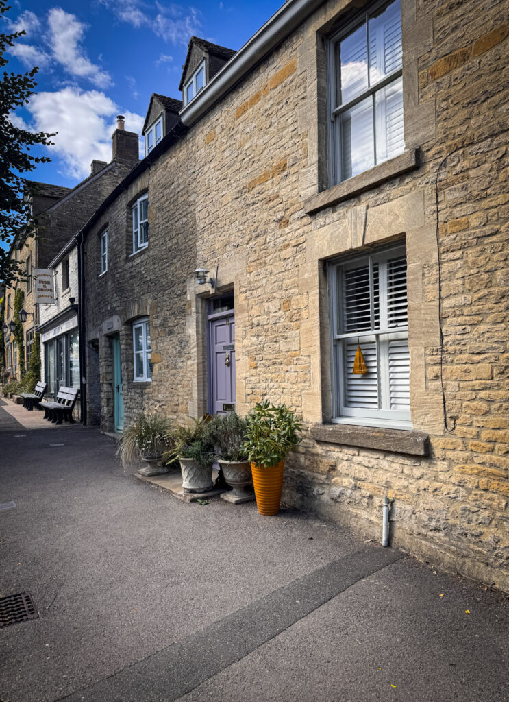 Top 5 Villages in the Cotswolds Quintessential limestone cottages featuring a lavender front door and grey window shutters next to a local fish and chip shop in Stow-on-the-Wold.