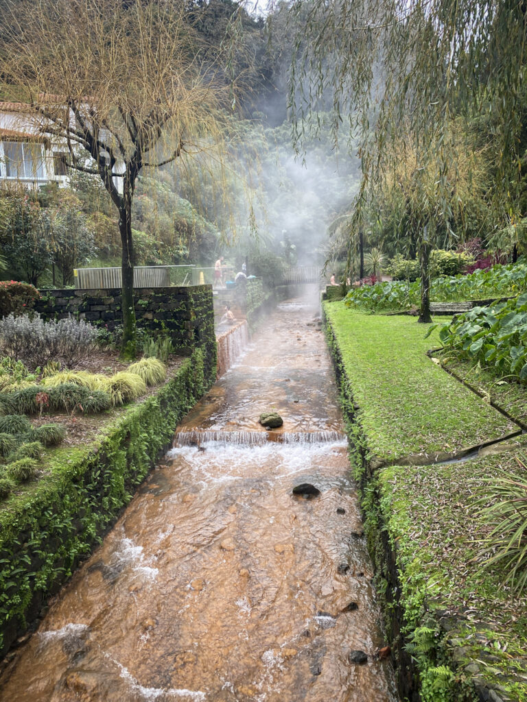 Top Things to Do in São Miguel, Azores Steam rising from an orange, iron-rich thermal river channeled through stone banks and lush tropical gardens at Poça da Dona Beija hot springs in Furnas, São Miguel, Azores.