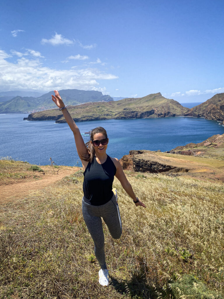 Madeira Travel Guide Ssmiling and running with one arm raised on a grassy trail overlooking the Ponta de São Lourenço bay in Madeira.