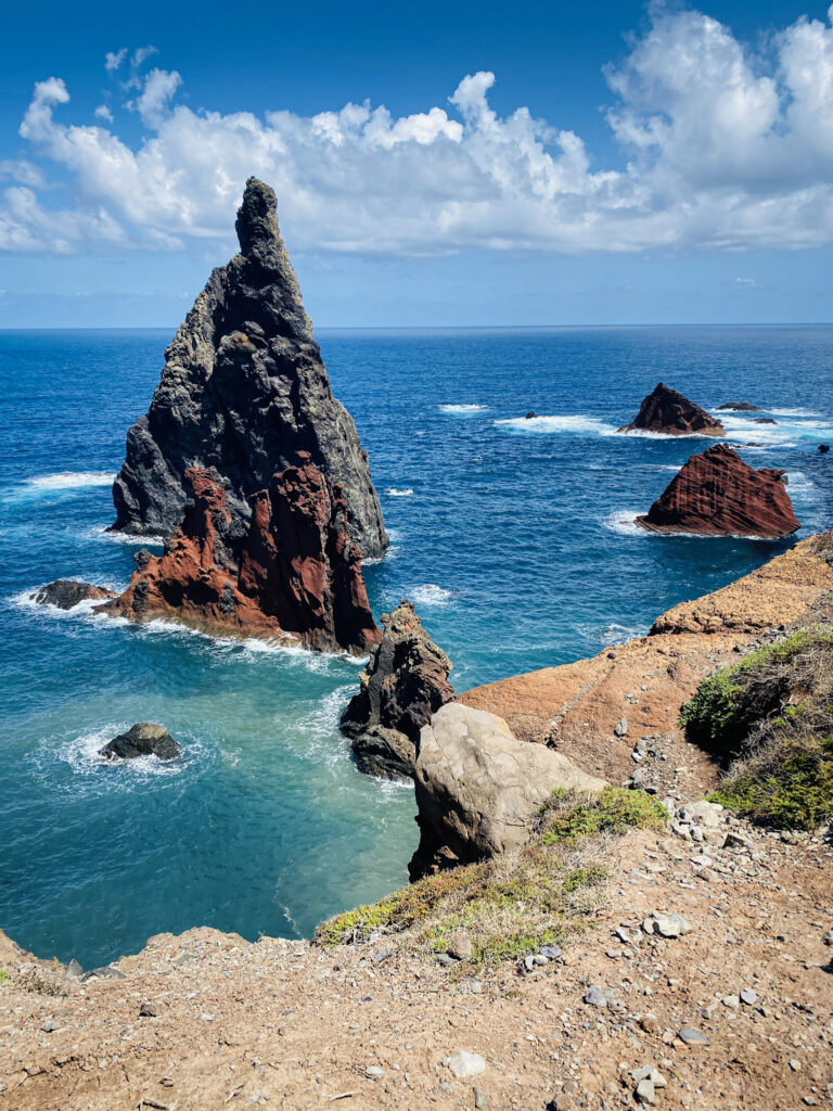 Madeira Travel Guide A towering jagged sea stack and distinct red volcanic rock formations rising from the blue ocean at Ponta de São Lourenço, Madeira.