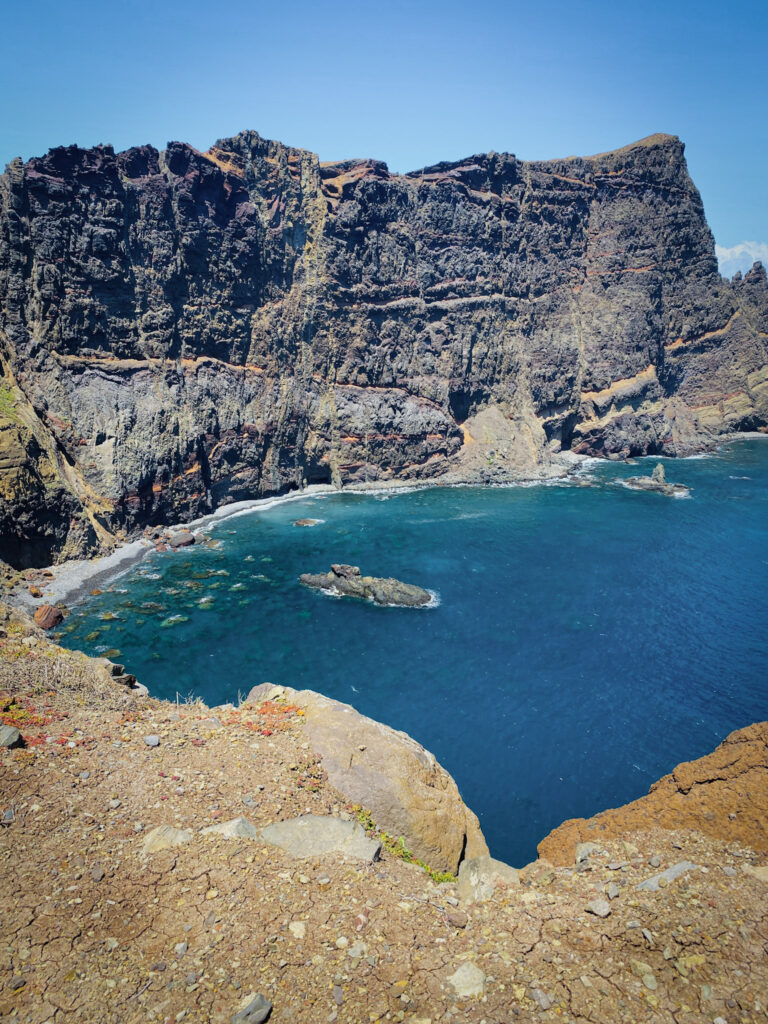Madeira Travel Guide Towering layered volcanic cliffs framing a deep blue ocean bay along the Ponta de São Lourenço peninsula in Madeira.