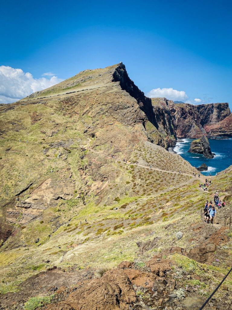 Madeira Travel Guide Hikers walking along a dirt trail on a rugged volcanic ridge leading toward a peak at Ponta de São Lourenço, Madeira.